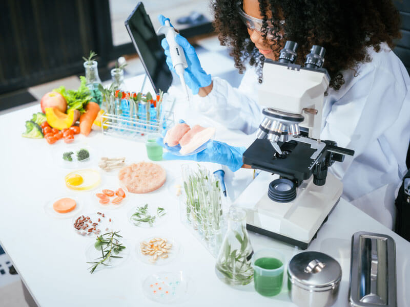 female scientist examining a meat sample under a microscope for nutrition analysis